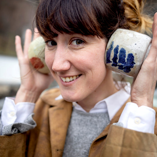 Happy artisan woman holding her pottery up to her ears to hear the ocean.