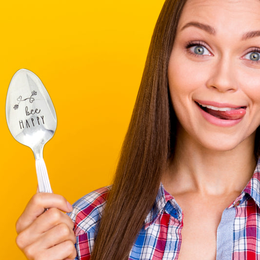 Cheerful lady hold an artisan made, hand stamped silver spoon with the text "Bee Happy"
